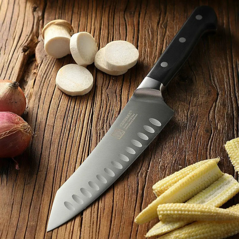 Couteau de chef élégant en acier inoxydable, doté d’un manche noir, avec des ouvertures découpées en forme d’ovales le long de la lame, reposant sur une surface en bois, dans le cadre d’un ensemble de couteaux de chef comprenant des ciseaux de cuisine en acier inoxydable.