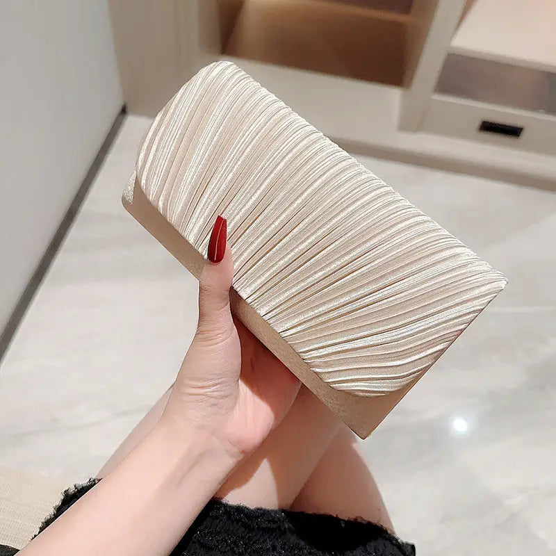 A sleek off-white pleated satin clutch with a glossy finish and subtle vertical ridges designed as a minimalist women’s evening bag.