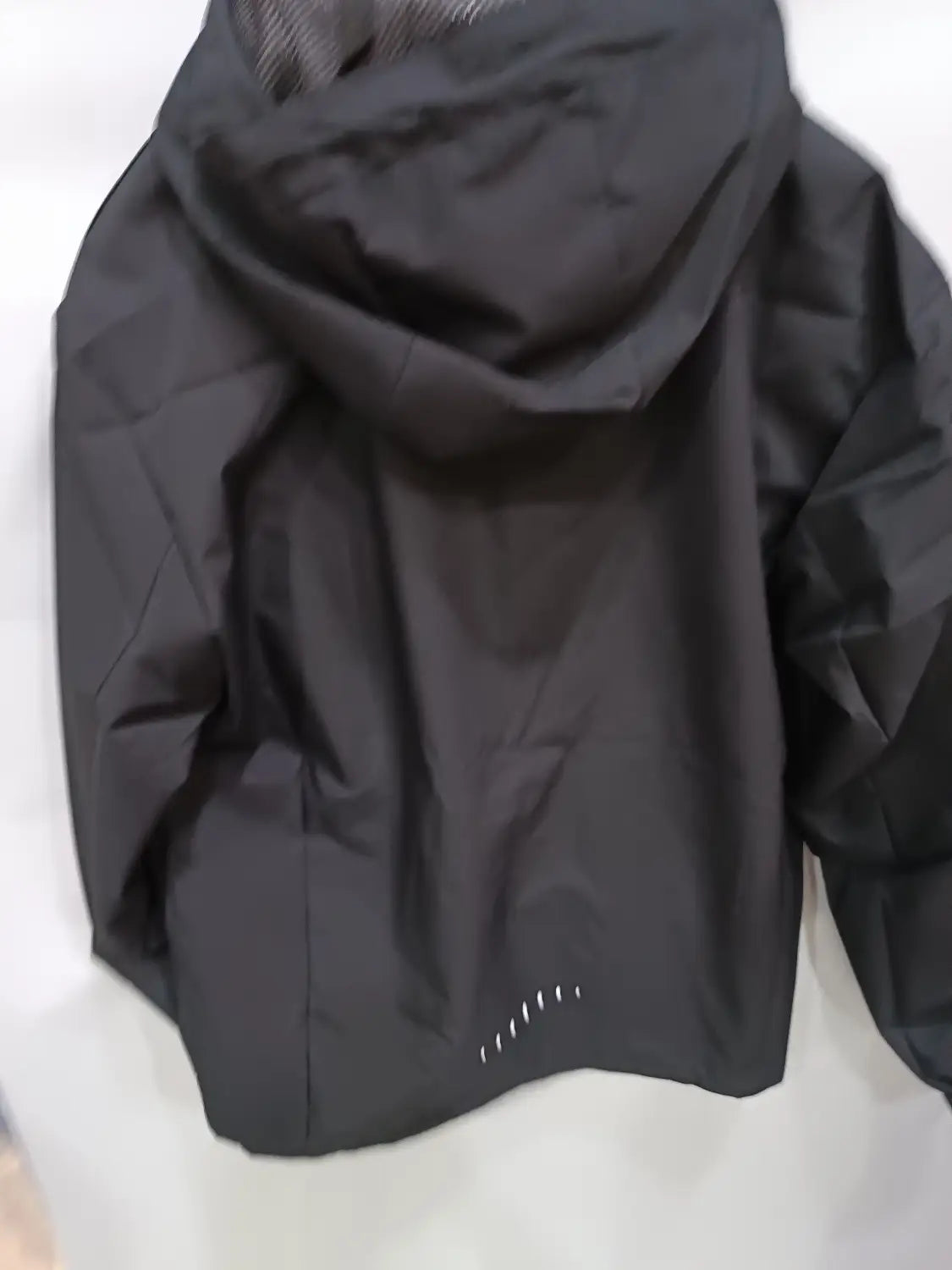 Black hooded waterproof hiking jacket for men featuring sleek lightweight fabric and subtle reflective stitching along the hem viewed from the back side.