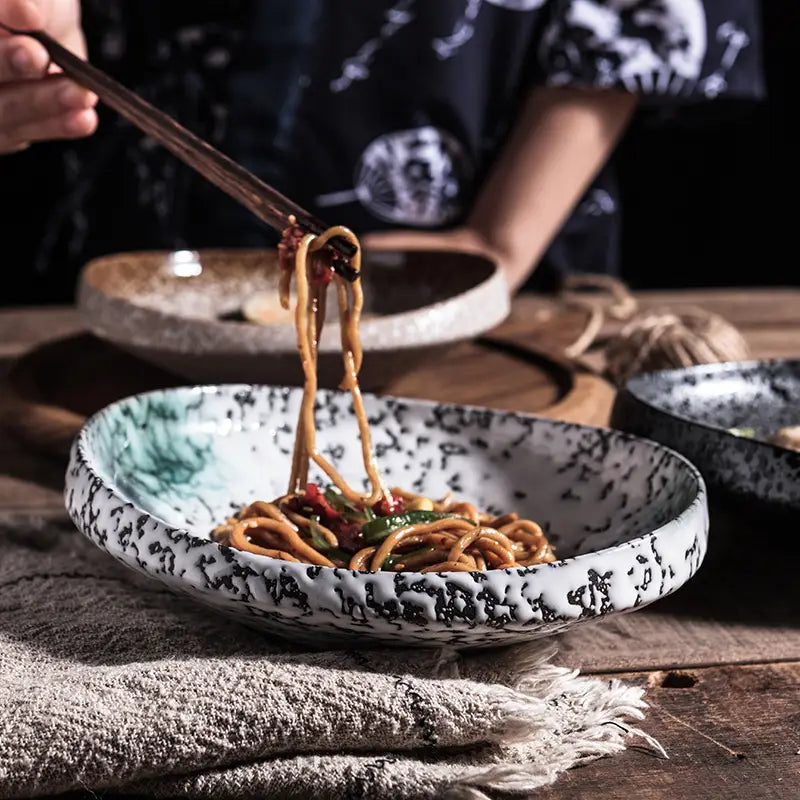 A white ceramic speckled serving bowl with a subtle green leaf design filled with noodles for home kitchens.