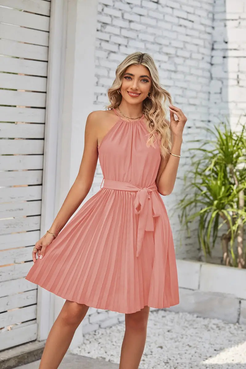 A soft pink sleeveless halter neck chiffon mini dress with a pleated skirt and matching belt tied at the waist.