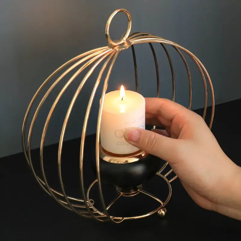 Gold geometric wire cage candle holder with black base holding a white pillar candle inside.