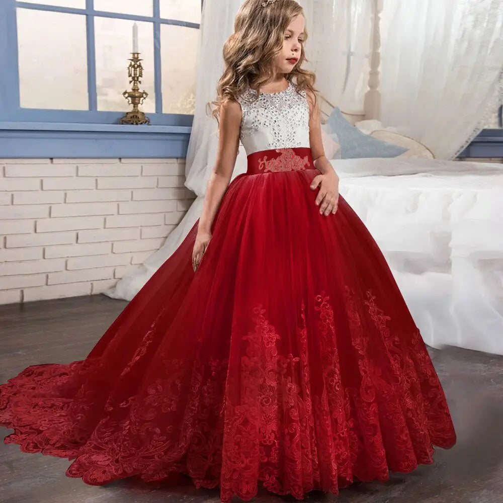 Ein junges Mädchen trägt ein mit Stickspitze verziertes Tüllblumenmädchen-Prinzessinnenkleid in Rot und Weiß mit detailliertem Mieder, Spitzenrock und passender Schärpe in der Taille.