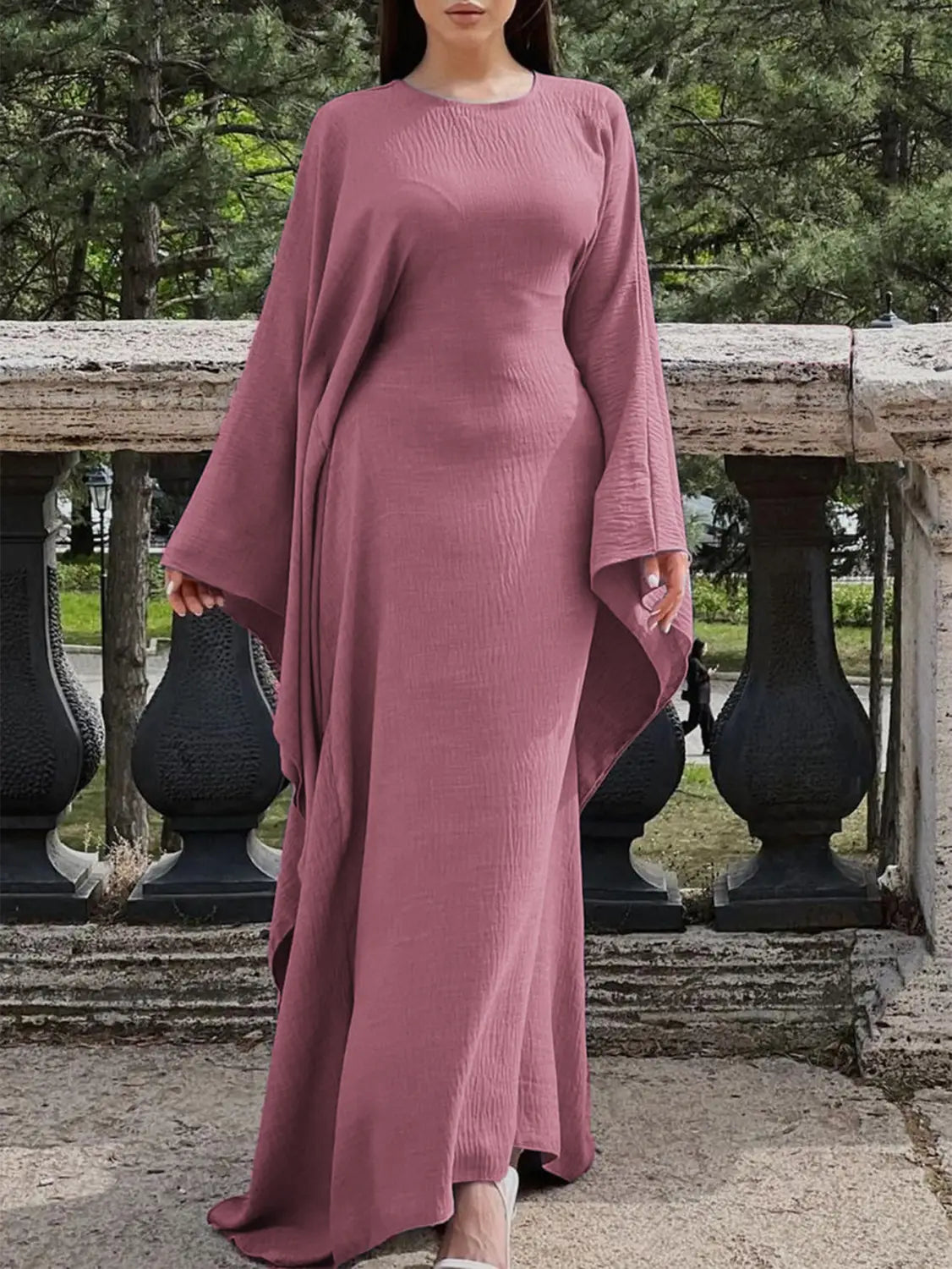 elegant long sleeve satin maxi dress in dusty rose with wide bell sleeves and a draped asymmetrical ruffled hemline