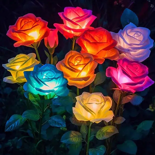 A cluster of illuminated solar garden lights featuring color changing artificial rose flowers in red orange yellow blue and pink.