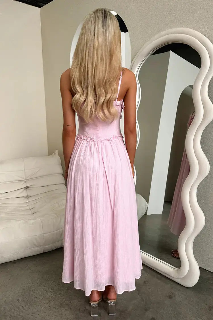 A flowing pale pink sleeveless maxi vacation dress with delicate ruffled detailing at the waist and thin spaghetti straps.