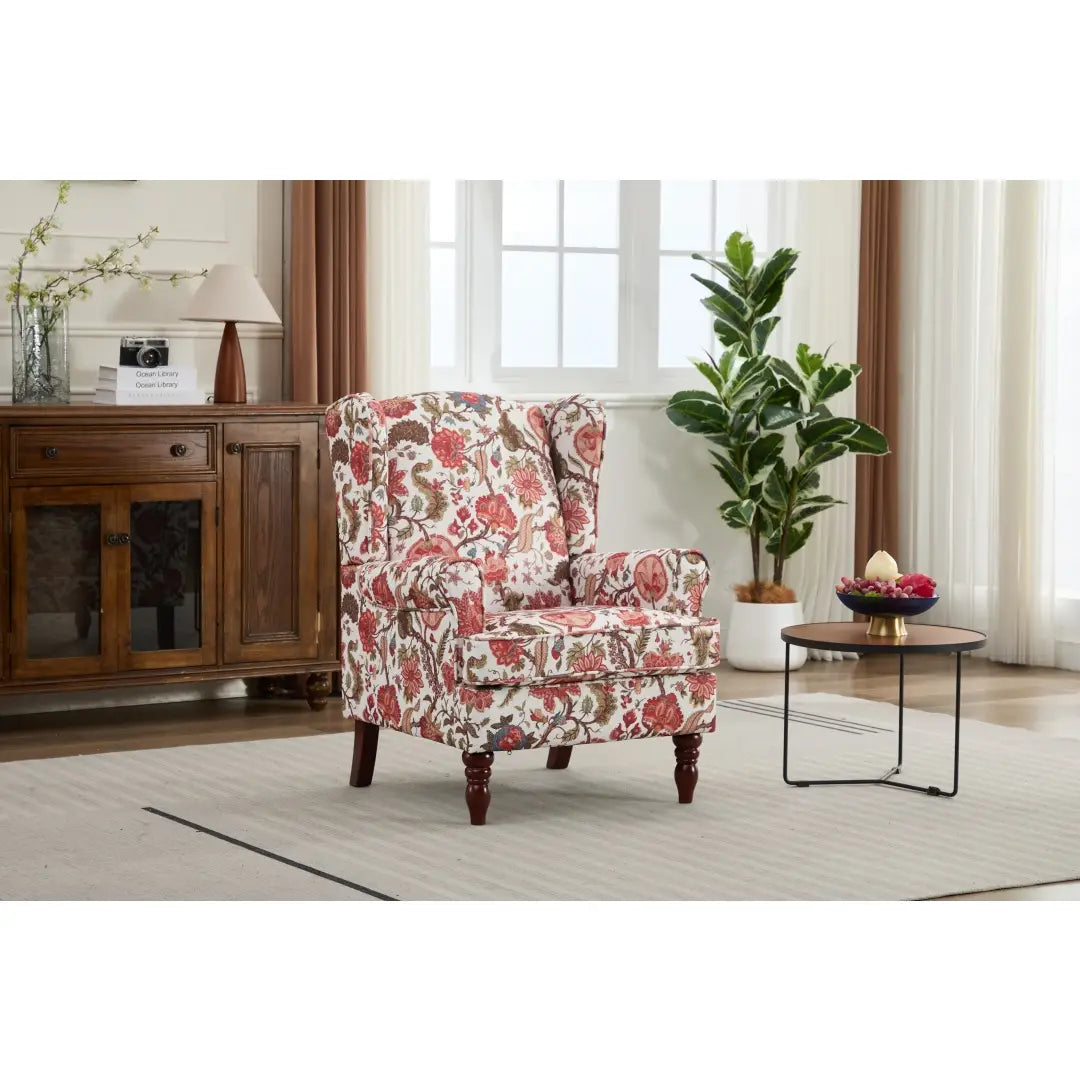 Una silla tipo ala con respaldo capitoné floral, tapizada en un tejido con flores rosadas rojas y beige sobre un fondo claro, con patas de madera retro.