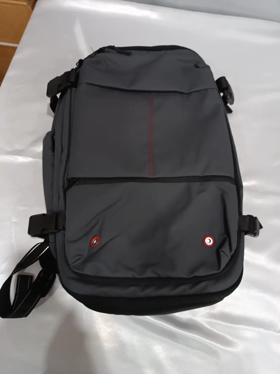 Dark gray travel backpack with black trim and red accent stitching featuring two circular brand logos on the front pocket designed for vacuum compression and business laptop use.