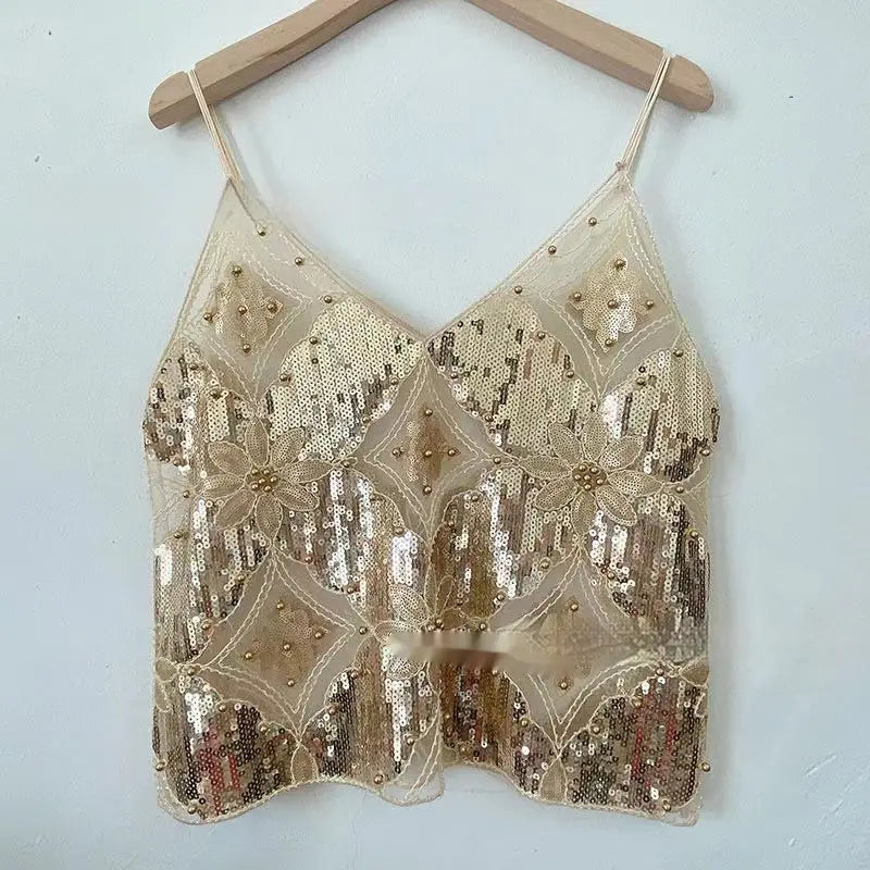 Ein schimmerndes goldfarbenes Pailletten-gesticktes Mesh-Camisole-Top mit zarter Blumeneinstickerei und perlenbesetzten Akzenten, hängend an einem Holzkleiderbügel.