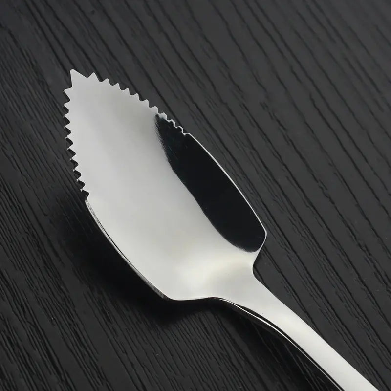 Cuillère à pamplemousse en acier inoxydable brillant, avec un bord dentelé en forme de feuille, conçu comme racloir à fruits.