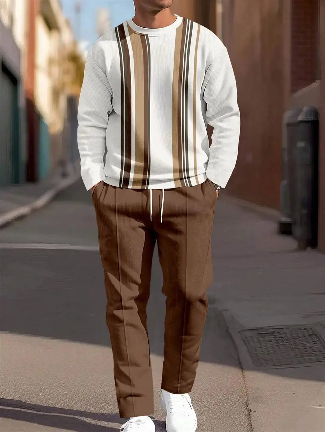 Un homme portant un ensemble sweat à carreaux et pantalon pour hommes, comprenant un sweat-shirt blanc avec des rayures verticales marron et noires sur la poitrine, associé à un pantalon marron assorti.