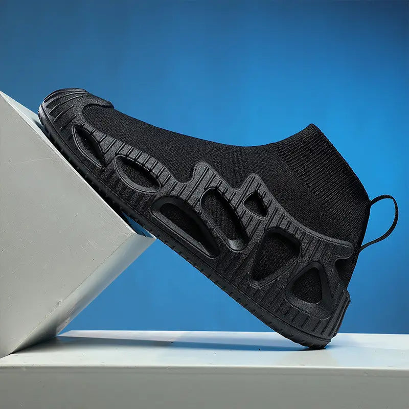 Schwarzer Strick-Sockensneaker mit strukturierter, gegossener Gummisohle mit Aussparungsmustern und integrierter Zuglasche für den lässigen, geschlechtsneutralen Einsatz.
