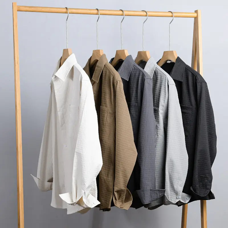 Une collection de cinq chemises homme décontractées à manches longues boutonnées, dans des tons neutres, avec une trame texturée subtile et un col classique.