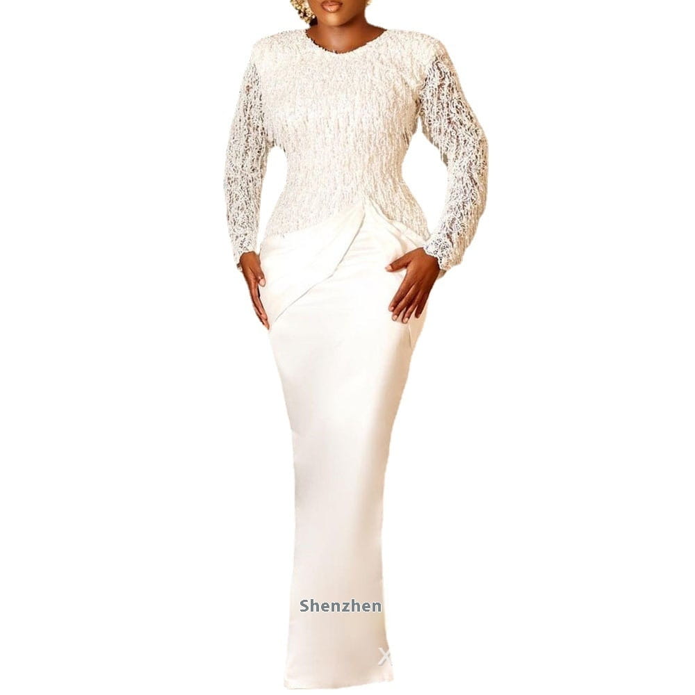 Une robe élégante blanche en dentelle et satin à manches longues avec glandé, à longues manches transparentes, un buste ajusté et une jupe fluide.