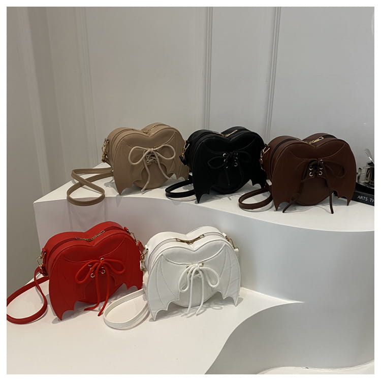 A collection of bat wing heart crossbody bags with lace up detail in red white beige black and brown featuring a heart shape and crossbody design.