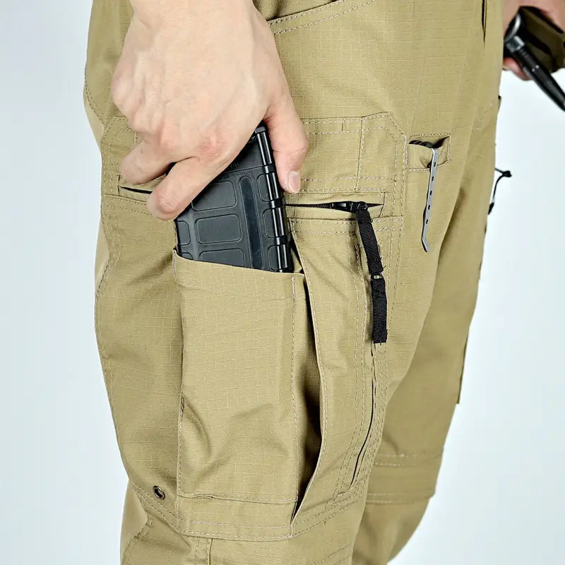 Pantalons tactiques P40 beige pour hommes, avec plusieurs poches, dont une contenant un chargeur en plastique noir, conçus comme des pantalons militaires robustes.