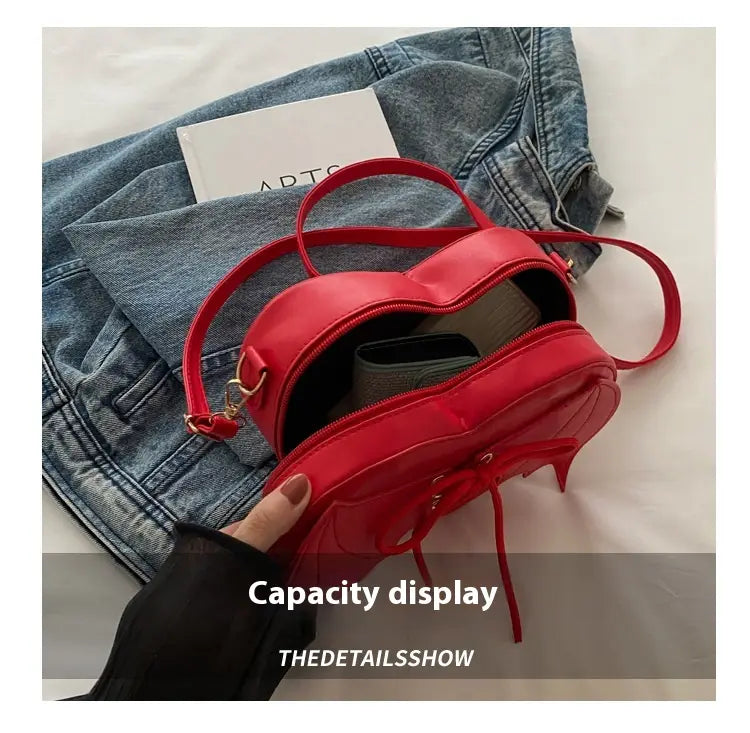 A vibrant red patent leather bat wing heart crossbody bag with lace up detail and matching straps.