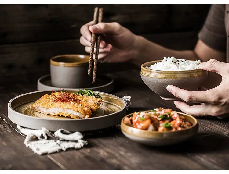 A rustic ceramic tableware bowl with a matte gray finish and subtle golden rim holding fluffy white rice garnished with black sesame seeds from a retro Japanese dinnerware set.