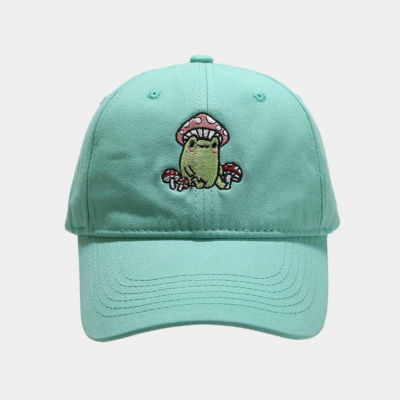 Mint green baseball cap featuring a cute embroidered frog sitting under pink and white mushrooms in a frog mushroom embroidered baseball cap design.