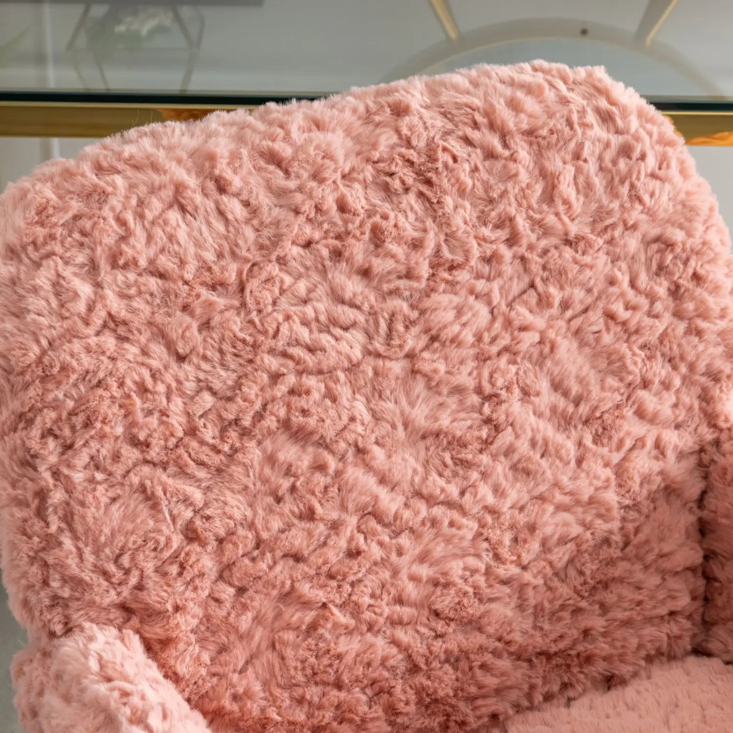 Une housse de chaise de bureau en fausse fourrure rose poudré, avec une texture souple et bouclée, montée sur un piétement en métal doré.