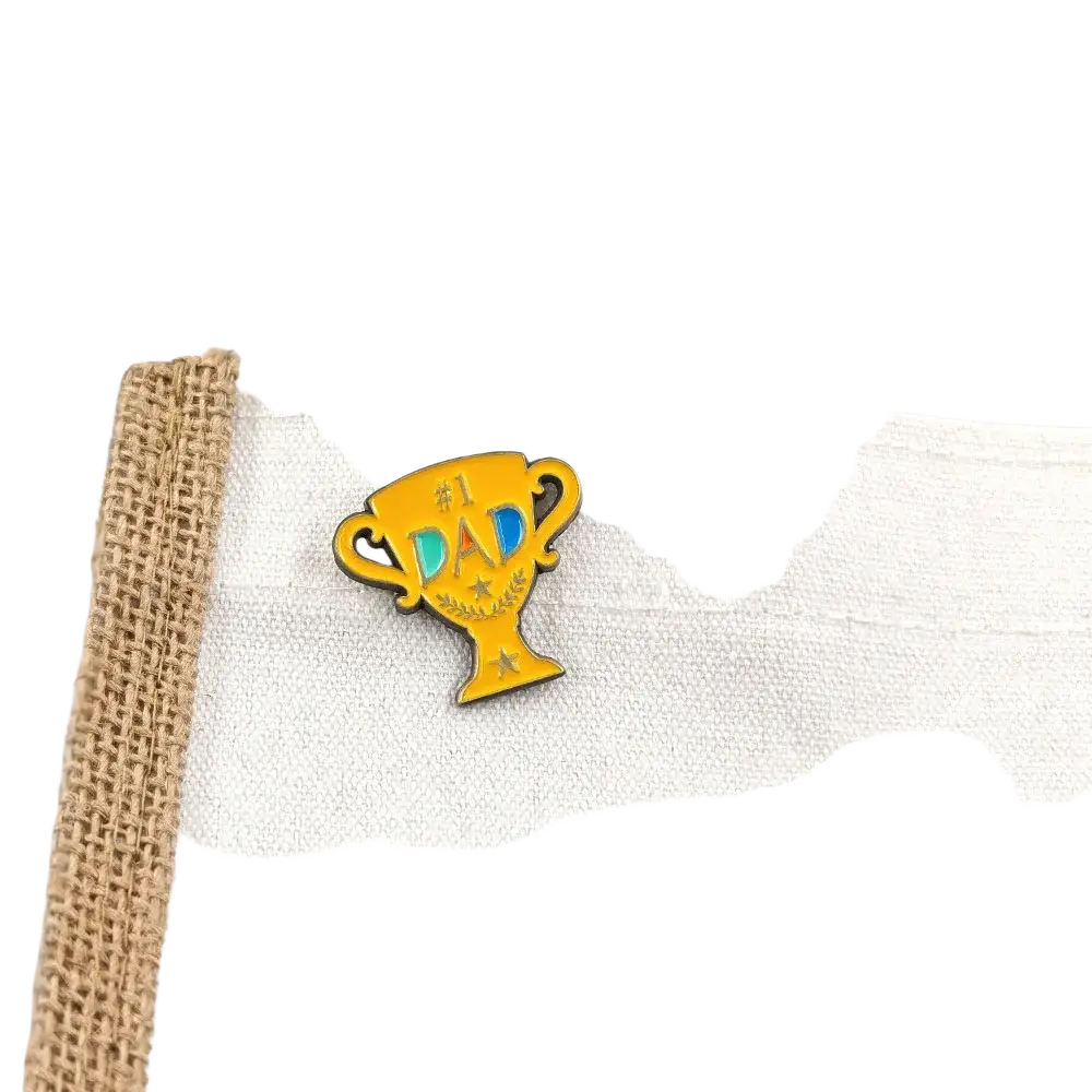 A vibrant yellow enamel pin shaped like a trophy with #1 dad text in blue and black and decorative stars
