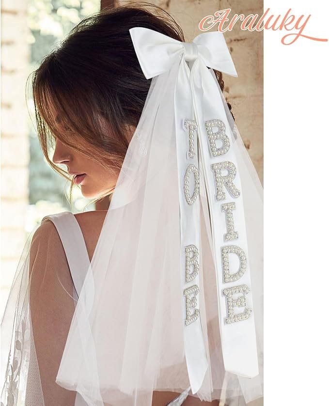 White bridal bow veil featuring a large satin bow and rhinestone bride to be lettering on the ribbon.
