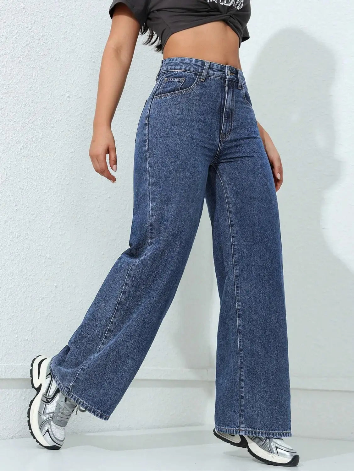 Jean en denim à taille haute, jambe large et évasée, en lavage bleu moyen, avec une couture classique et des passants de ceinture.