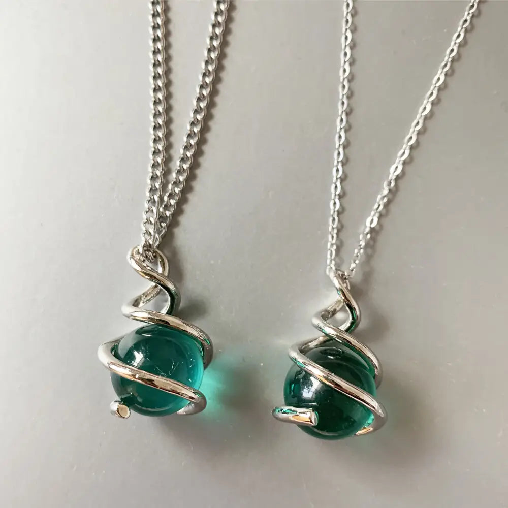 Collares con colgantes de esfera de vidrio verde esmeralda y plata en forma de espiral, con alambre de plata retorcido que encierra la pieza y cuelga de delicadas cadenas.