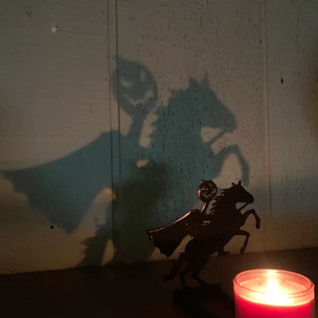 A black metal silhouette of a figure riding a horse casting a dramatic shadow on the wall behind in a halloween bat candle holder black metal shadow decor.
