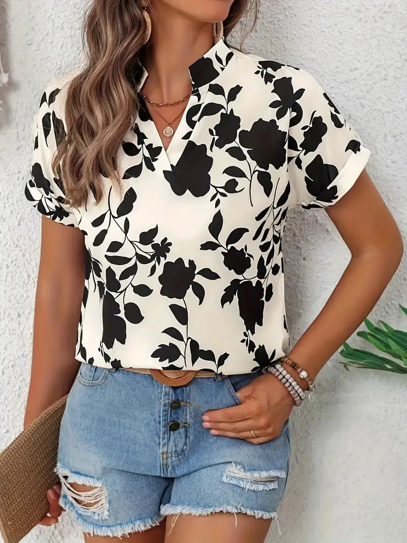 A woman wearing a black and white floral print short-sleeved stretch satin blouse with a v-neck and collar.