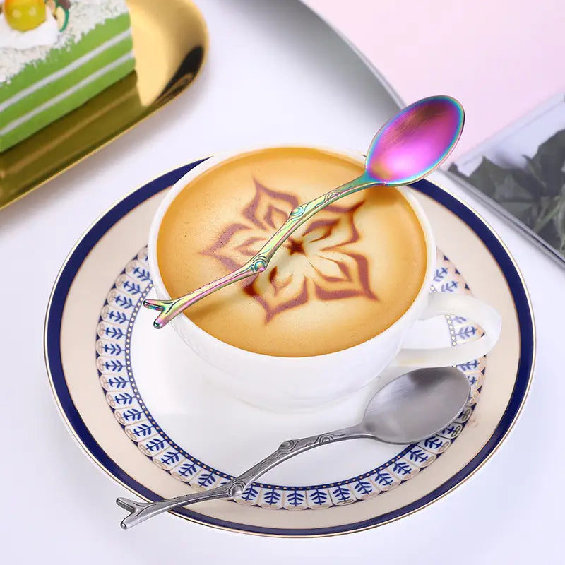 Cuillère en acier inoxydable irisée, au manche en forme de feuille, provenant de l’ensemble d’ustensiles de dessert en acier inoxydable à branches, posée dans une tasse de latte art