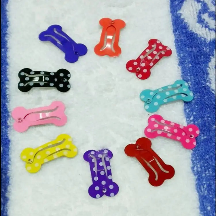 A set of colorful bone-shaped metal dog hair clips featuring solid and polka-dotted glossy plastic surfaces for pet styling.