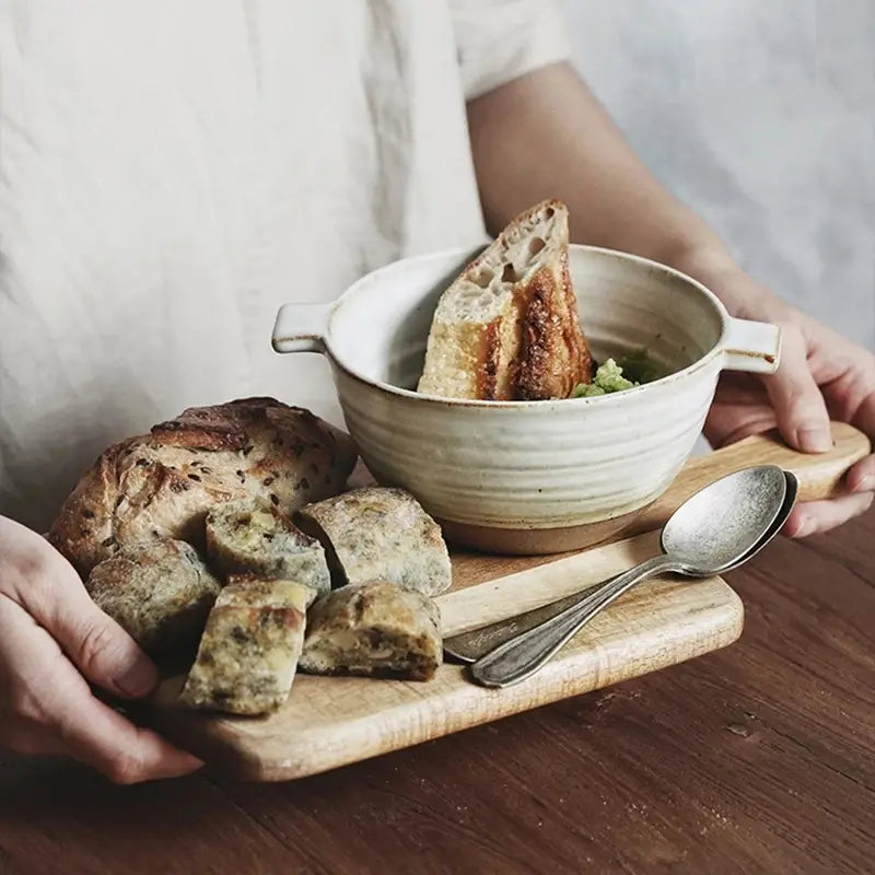 A rustic off-white 6 inch binaural Japanese stoneware ceramic soup bowl with subtle horizontal ridges holds a piece of toasted bread.