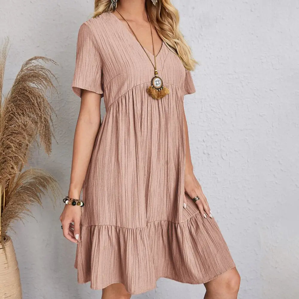 Une robe d’été souple rose poudré pour femmes, à encolure en V, à volants superposés, à manches courtes et avec des plis verticaux.