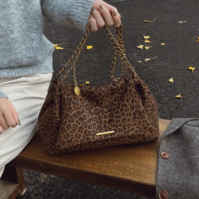 Brown leopard print crossbody bag with gold chain strap and small oval metal tag.
