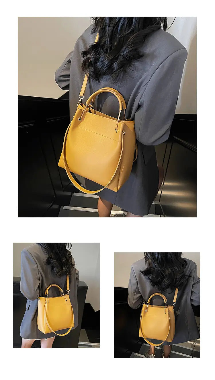 A mustard-yellow minimalist leather bucket bag with a structured rectangular shape, featuring top handles and an adjustable detachable shoulder strap.