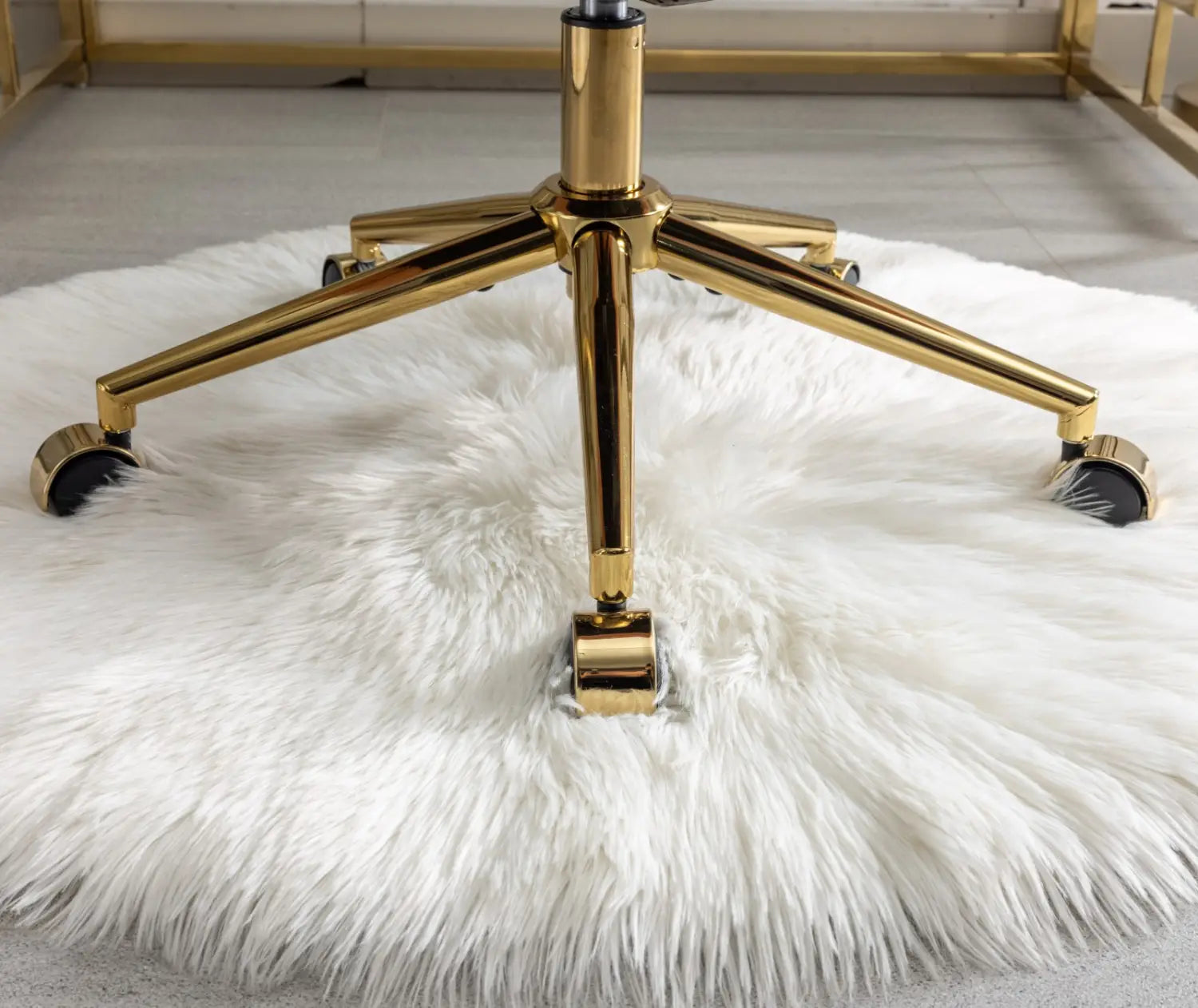 Un piétement cinq branches finition dorée avec des roues à roulettes noires d’une chaise de bureau en fausse fourrure rose, posée sur un tapis en fausse fourrure blanche.