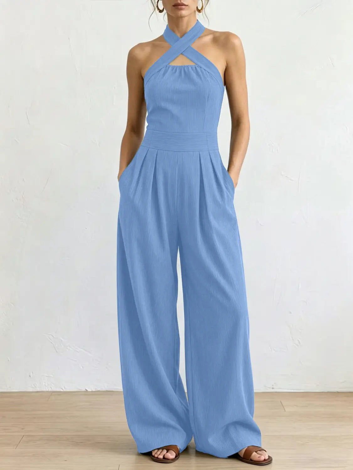 Ein hellblauer ärmelloser Halterneck-Jumpsuit mit weitem Bein, mit gekreuztem Frontausschnitt und fließenden Hosen im weitem Bein.