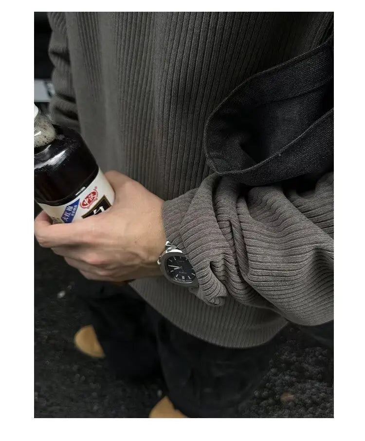 Un reloj elegante de tono plateado con esfera negra y diseño minimalista, llevado en la muñeca, combinado con una sudadera tipo jersey acanalada de media cremallera para hombre.