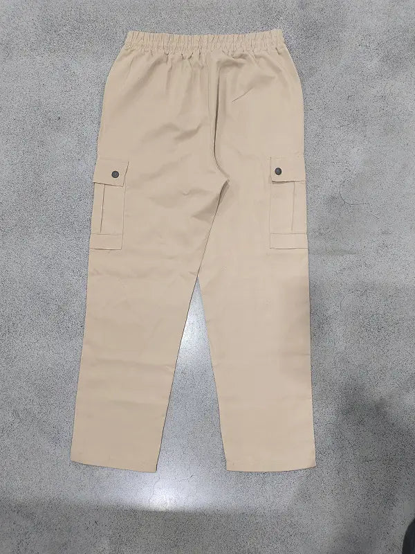 Beige mens straight leg cargo work pants featuring an elastic waistband and flap pockets secured by black buttons.