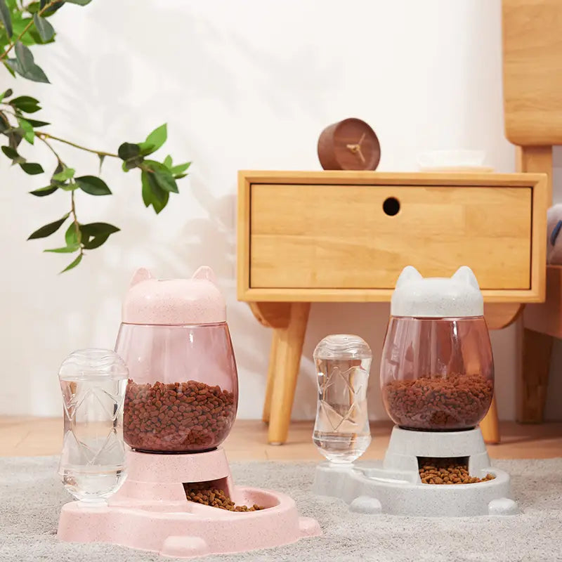 Automatic cat feeder and water fountain featuring pink and white cat-shaped design with transparent bowls filled with kibble.