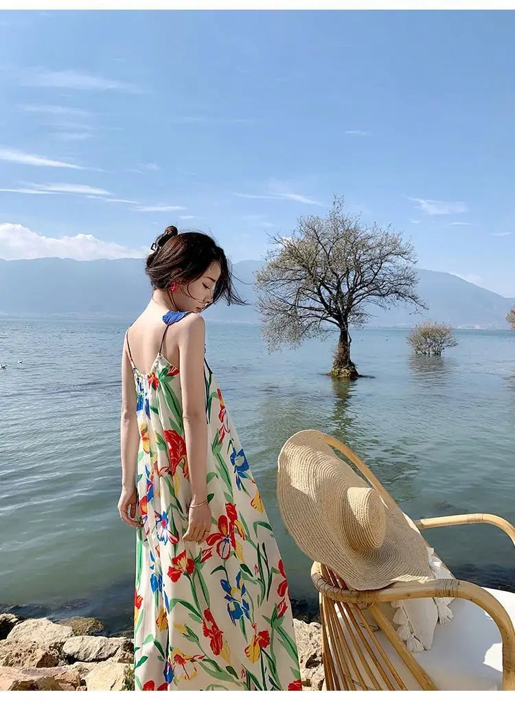 A woman wears a floral mesh maxi dress with a retro slip silhouette featuring vibrant red blue and green floral patterns on an off-white background.