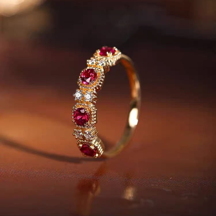 An 18k gold plated band ring featuring five vibrant pigeon blood red rubies set in ornate scalloped bezels accented with sparkling clear diamonds.