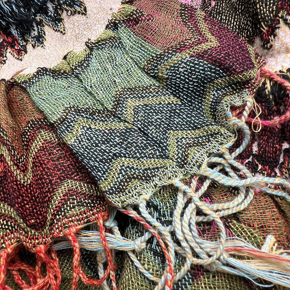 Écharpe en tricot géométrique tissé aux tons verts, noirs et bordeaux évoquant la terre, avec des franges rouges aux extrémités.