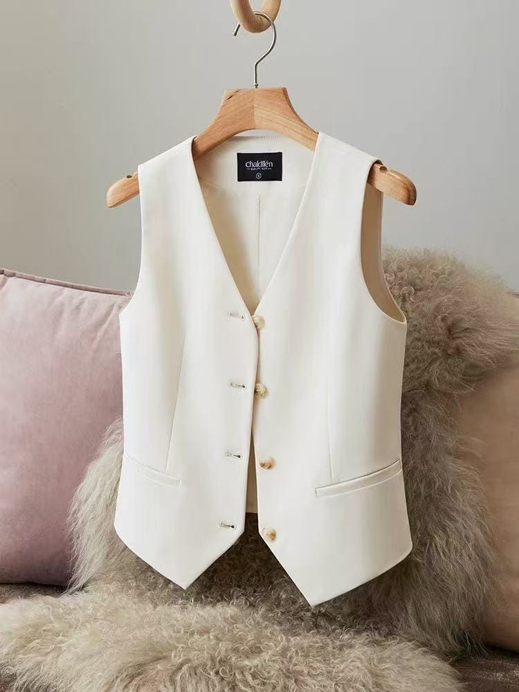 Eine ecrufarbene Polyester-Damenweste mit V-Ausschnitt und Verschlüssen vorne mit Knöpfen, die an einem Holzkleiderbügel hängt.