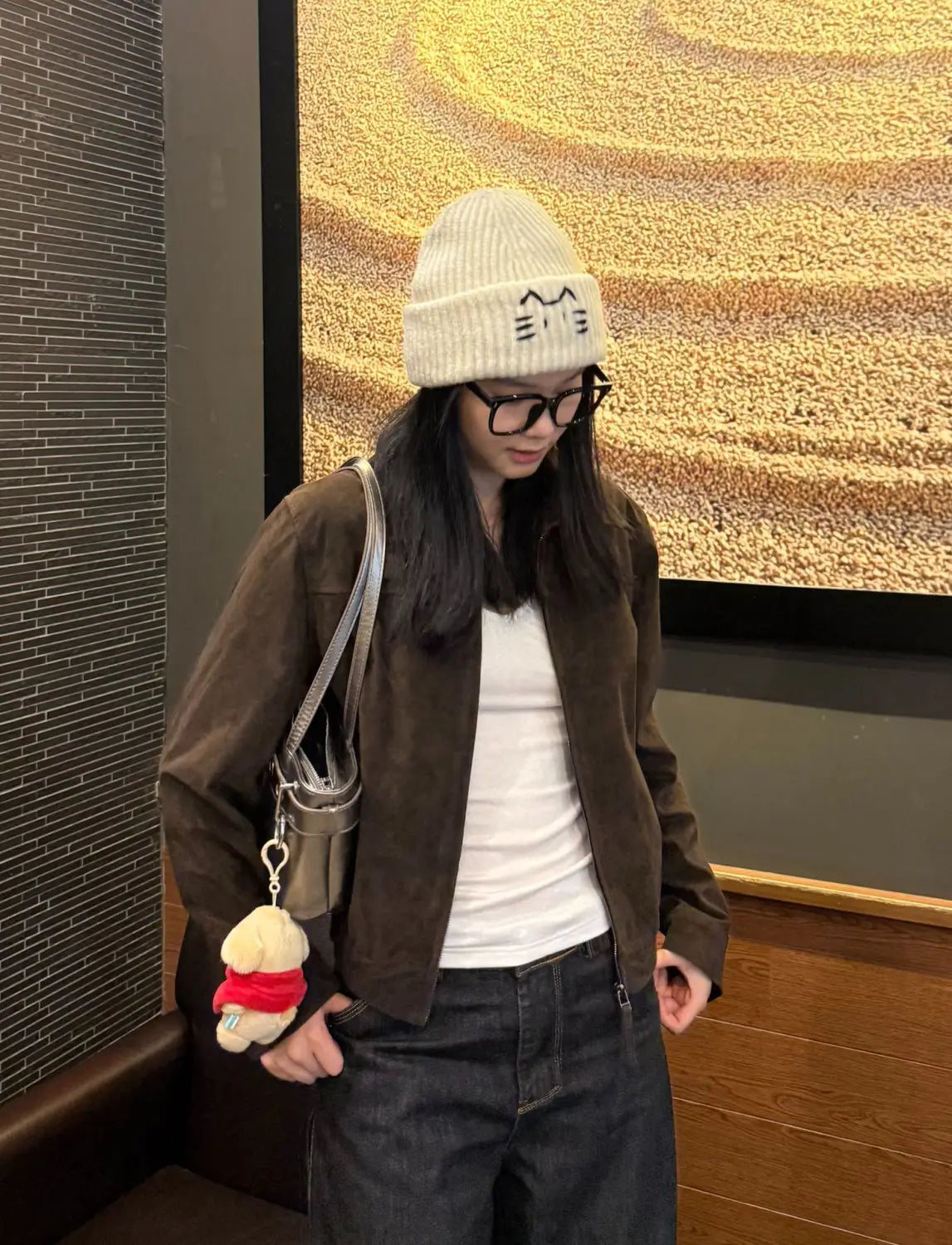 Cream-colored knitted beanie hat featuring a simple embroidered cat face design.