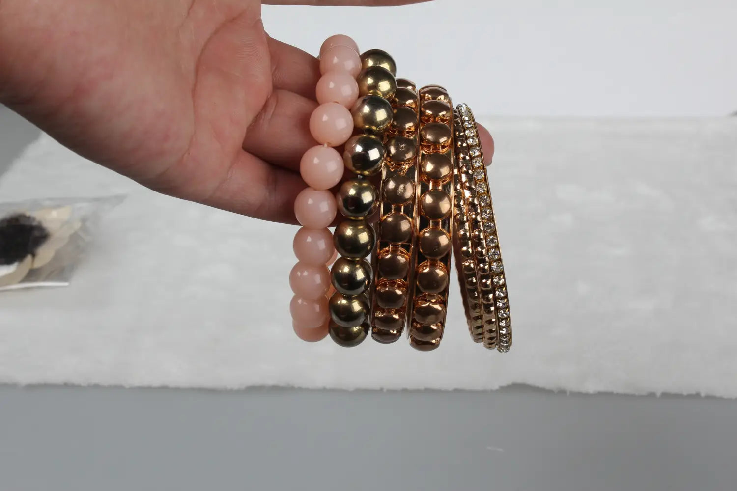 A hand holds a retro gold and pink rhinestone bangle bracelet set featuring soft pink beads, metallic gold-toned spherical beads, and intricate gold bangles with clear rhinestones and textured patterns.