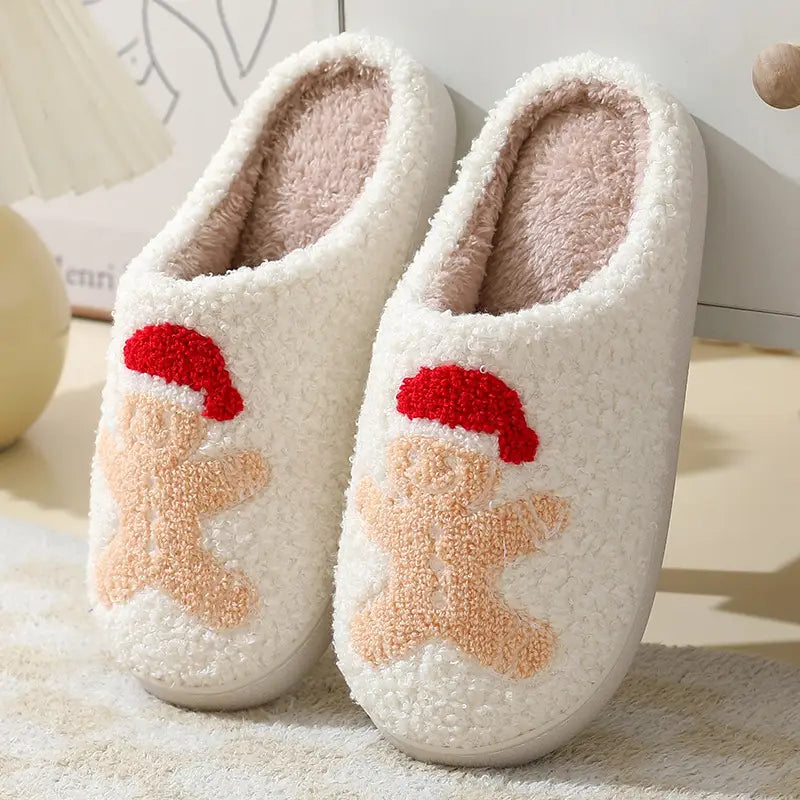 White fuzzy slippers with a beige gingerbread man embroidered on the front wearing a red Santa hat designed for festive winter use.
