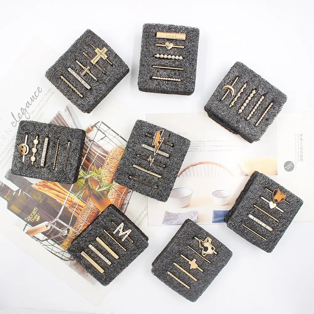 Set of eight gold-toned bar-style hairpins with silicone strap embellishments packaged in black foam featuring decorative designs including crosses lightning bolts and hearts.
