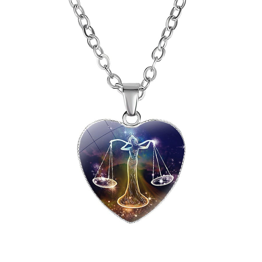 Heart-shaped pendant necklace with a silver-toned chain featuring a glossy illustrated design of the Libra zodiac symbol against a cosmic background with sparkling stars.
